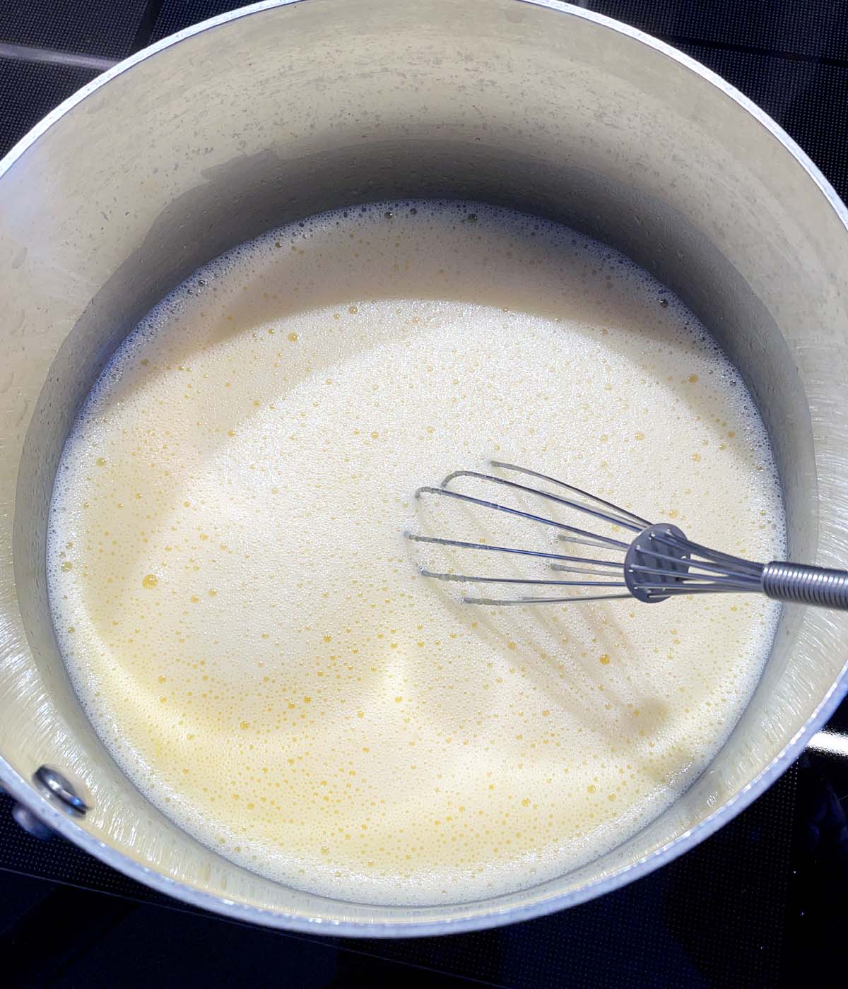 A metal pot containing a whisk and foamy yellow liquid.