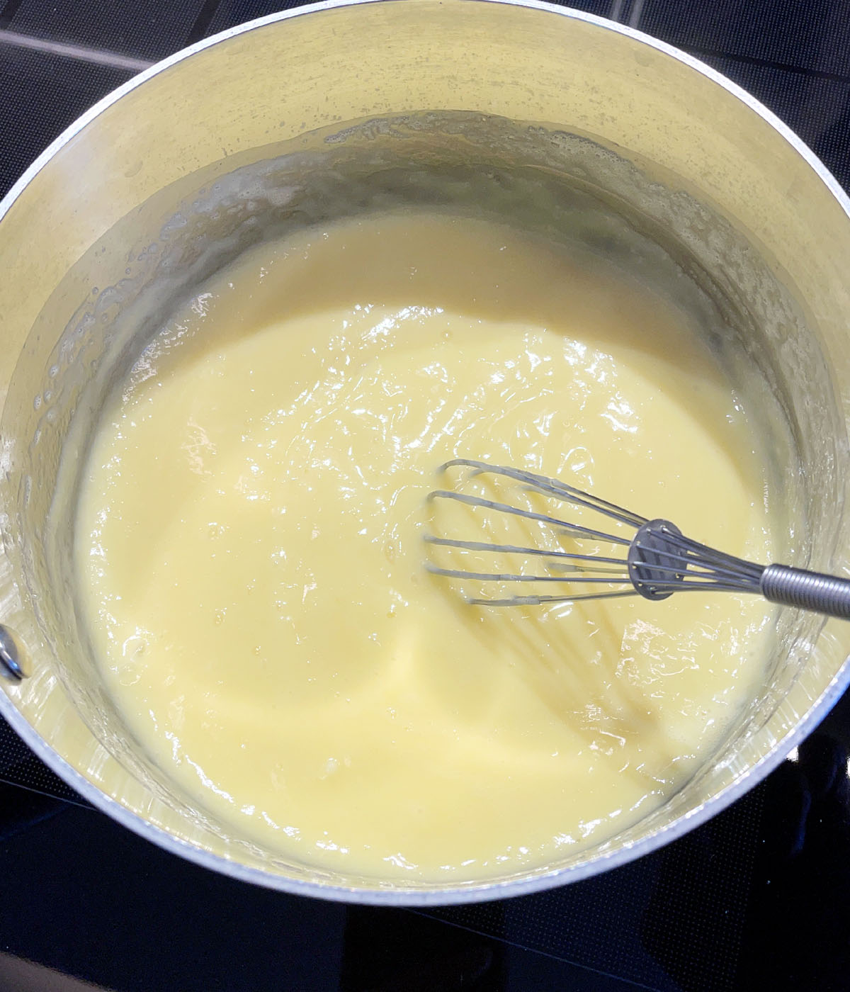 A metal pot containing thick yellow pudding and a whisk.