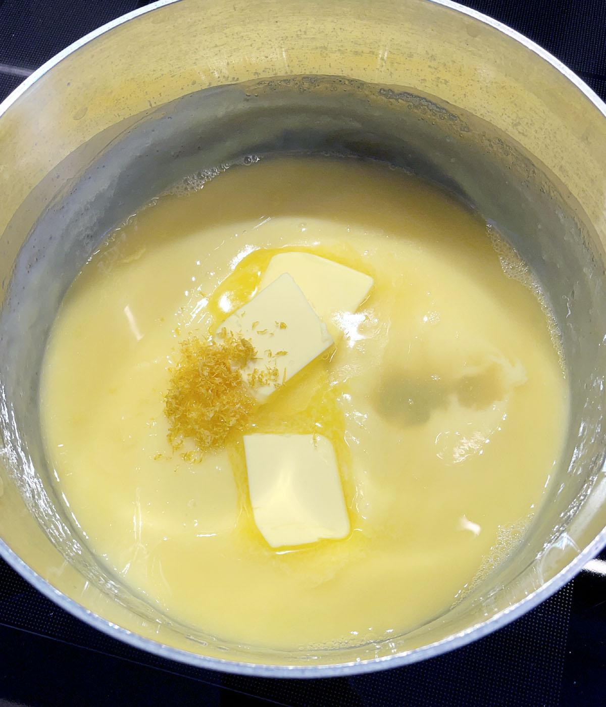 A pot containing yellow pudding, melting butter, yellow lemon zest.