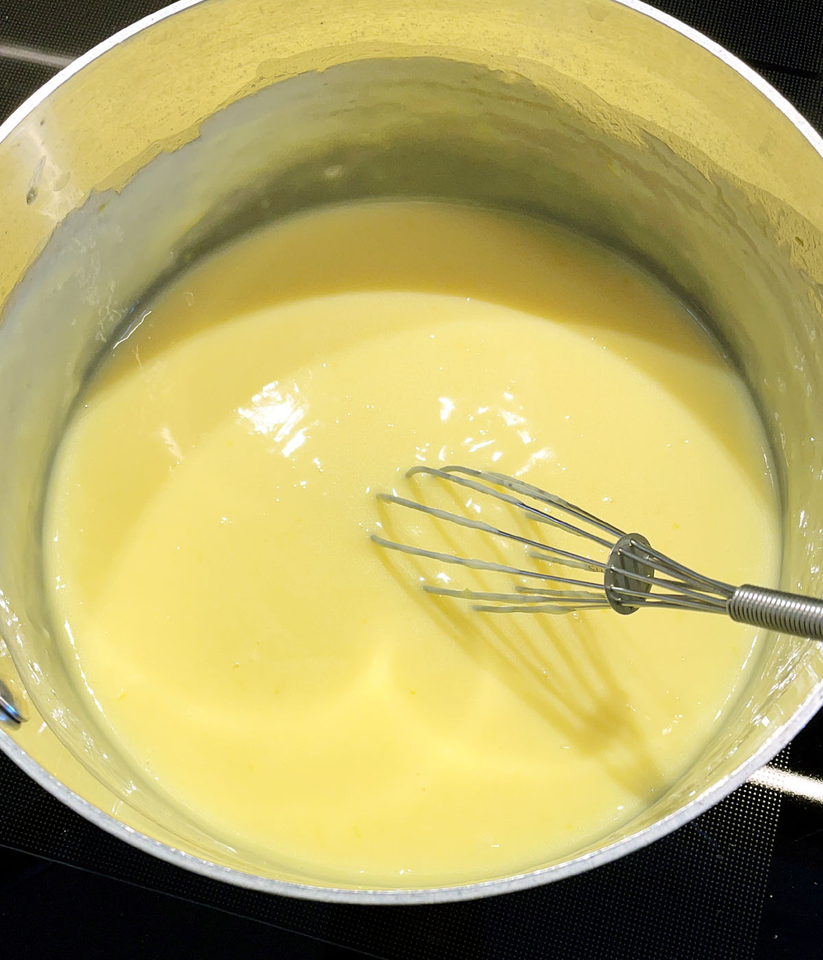 A whisk in a pot containing yellow pudding.