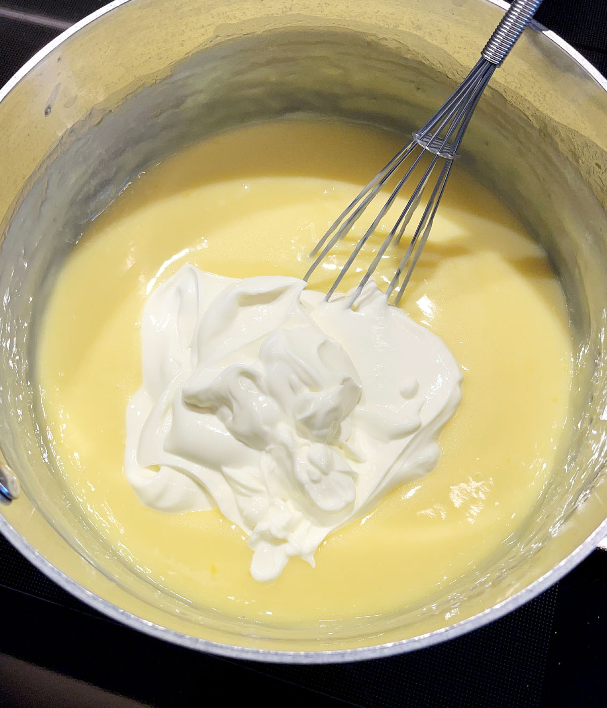 White yogurt added to a pot of lemon pudding.