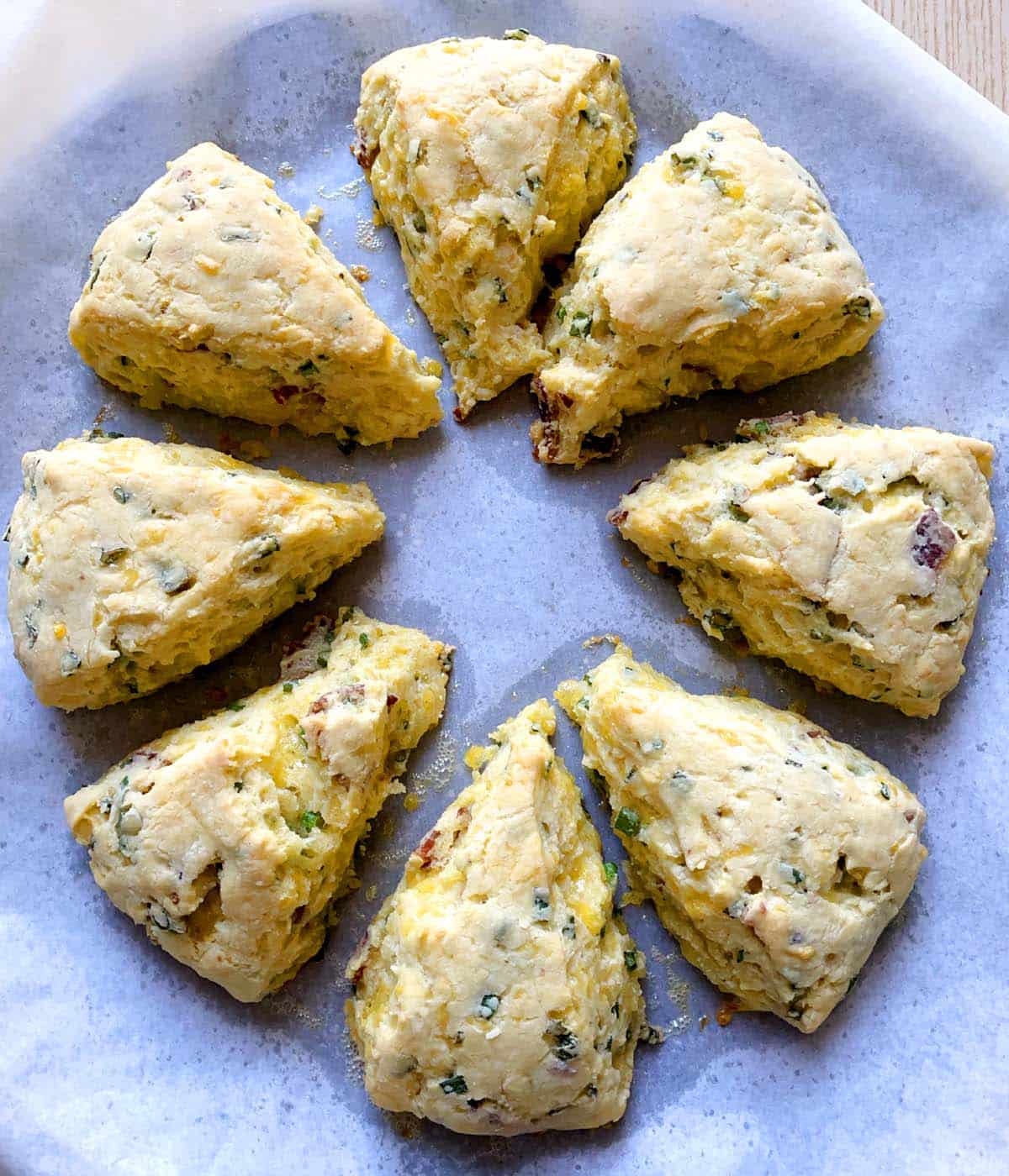 Baked bacon cheddar scallion scones on a white paper lined baking sheet.