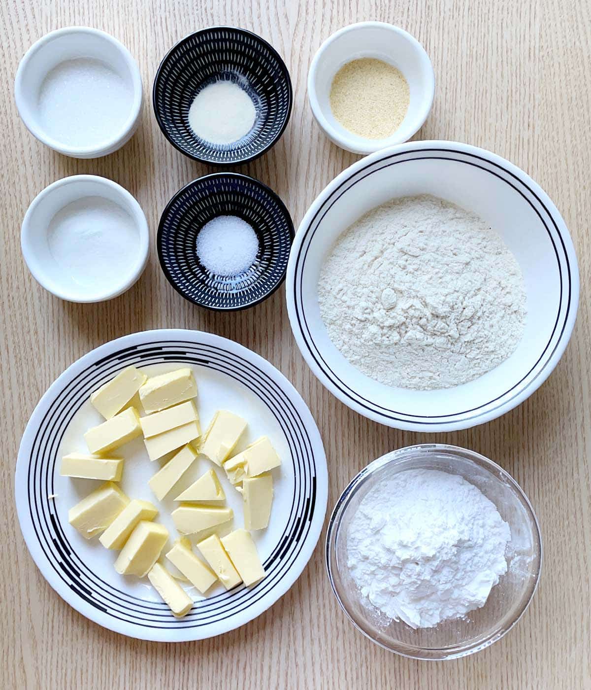 A white plate with chunks of yellow butter and seven bowls containing dry ingredients for scone dough.