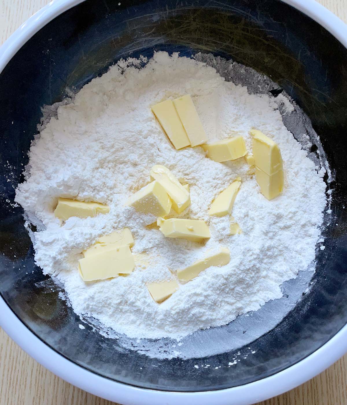 A round black bowl containing white flours and chunks of yellow butter.