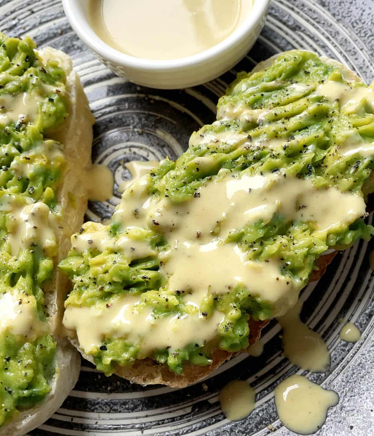 Two slices of toast topped with green mashed avocado and yellow honey mustard dressing.
